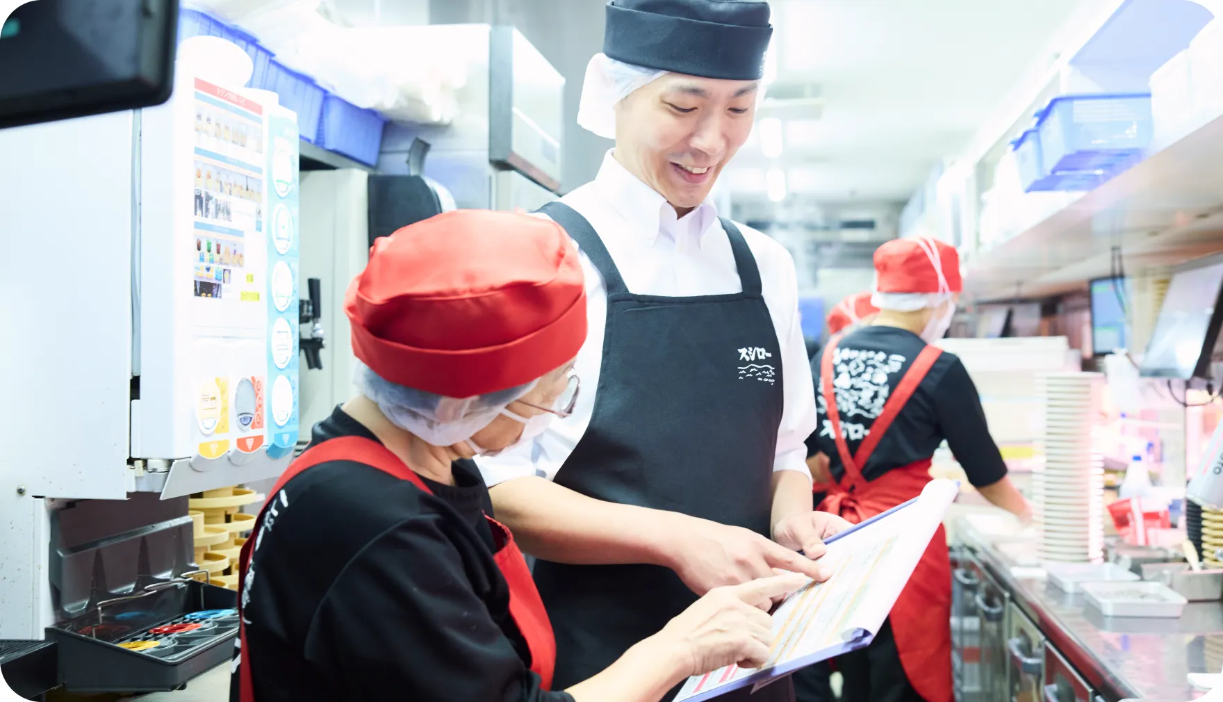 厨房でスタッフと資料を見ながら話す佐藤圭介